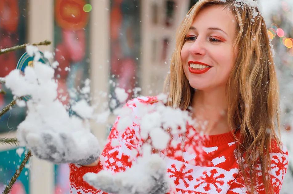 smiling woman in christmas sweater playing with snow