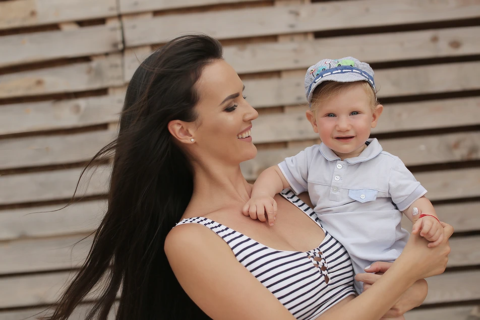 Smiling mother holding her baby outdoors, representing post-pregnancy body confidence after mummy makeover